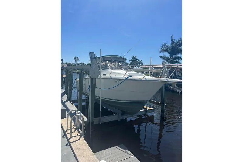Slide: The Image of 2000 Shamrock 290 Walkaround boat docked on a lift under clear blue sky. - 12
