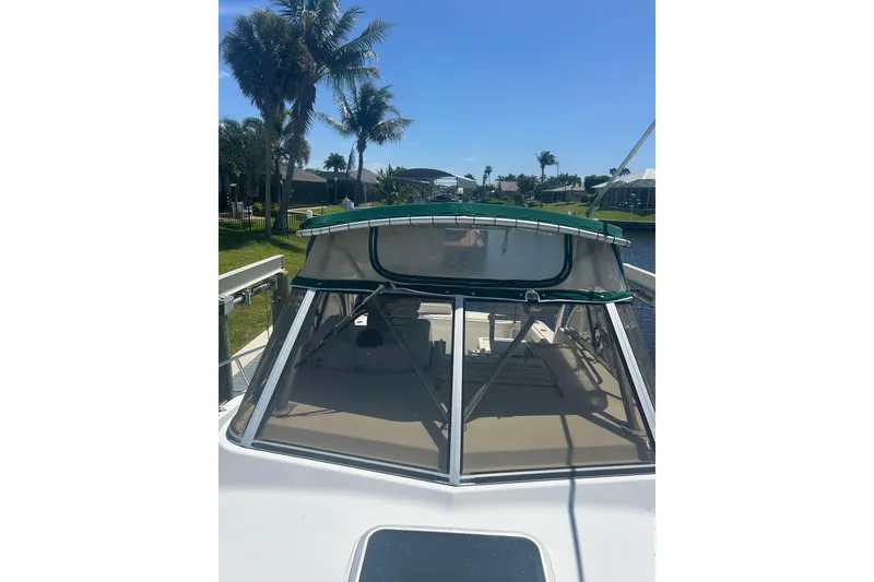 Slide: The Image of 2000 Shamrock 290 Walkaround boat with green canopy, docked near palm trees. - 14