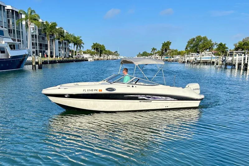 The Image of 2012 Stingray 234 LR boat cruising in a sunny canal with palm trees. - 0