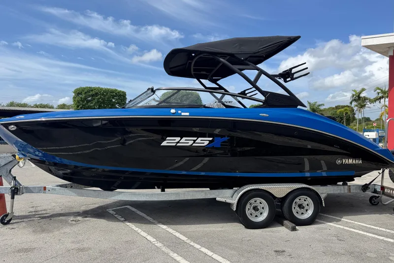 Slide: The Image of 2026 Yamaha Boats 255XD on trailer, sleek black and blue design, parked outdoors. - 3