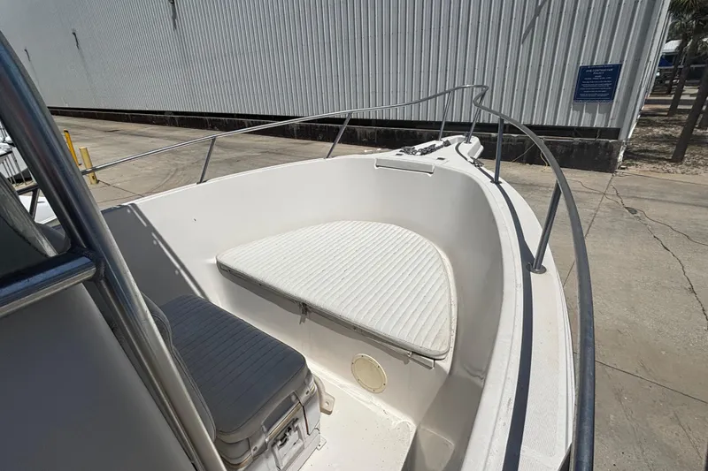 Slide: The Image of 2003 Robalo R230 Center Console boat with cushioned seating, docked near a metal building. - 4