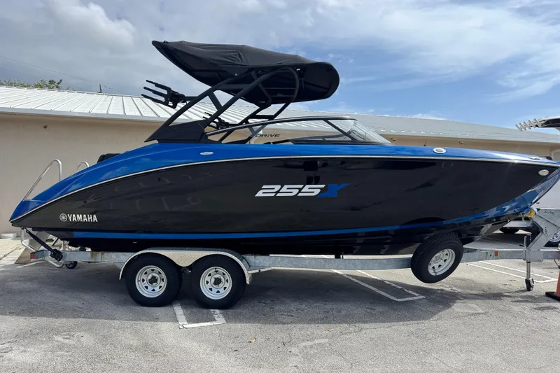 The Image of 2026 Yamaha Boats 255XD on trailer, sleek black and blue design, parked outdoors. - 0