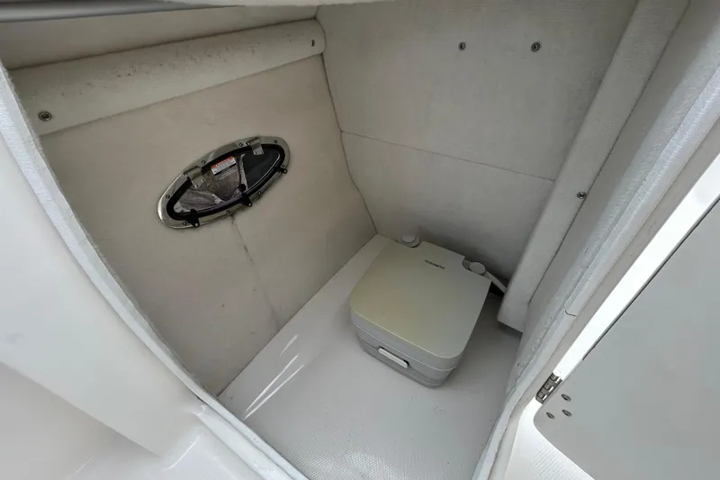 Slide: The Image of 2020 Chaparral 230 Suncoast boat interior with portable toilet and small window. - 94