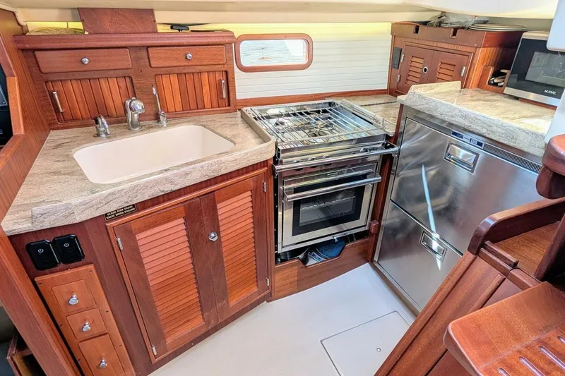 Slide: The Image of Island Packet 349 yacht kitchen, 1999 model, featuring wooden cabinetry, sink, stove, and stainless steel appliances. - 17