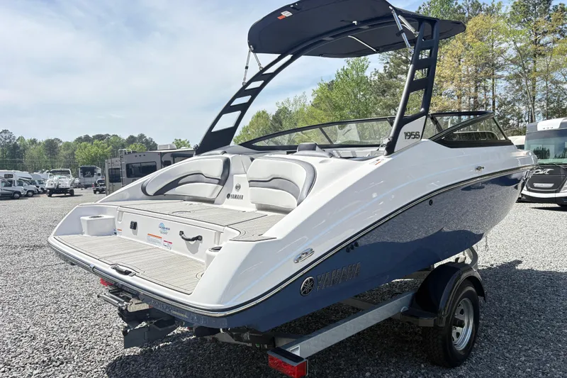 Slide: The Image of 2024 Yamaha Boats 195S, sleek design, blue and white, parked on gravel lot. - 3