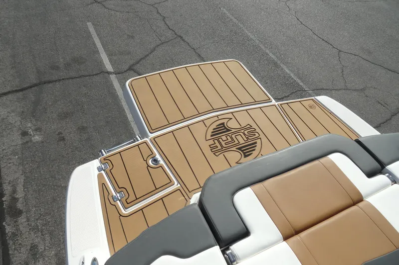 Slide: The Image of 2023 Chaparral 23 Surf boat deck with tan and gray seating, parked on asphalt. - 24