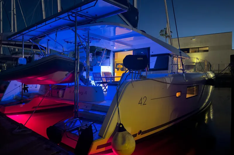Slide: The Image of 2018 Lagoon 42 catamaran illuminated with colorful lights at night in a marina. - 11