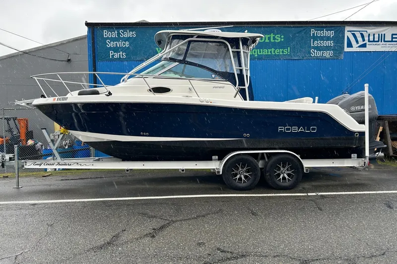 The Image of 2011 Robalo R265 Walkaround boat on trailer, parked outside a marine service shop. - 0