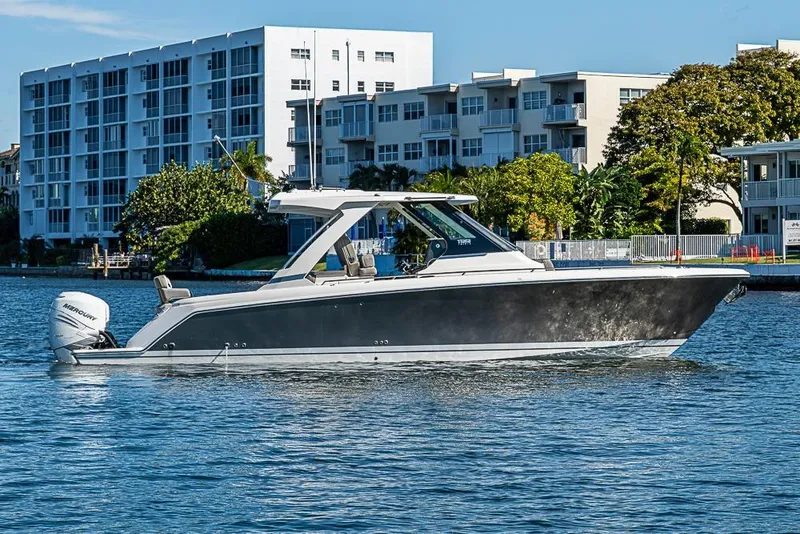 Slide: The Image of 2023 Tiara Sport 34 LS boat cruising on a sunny waterfront near modern buildings. - 66