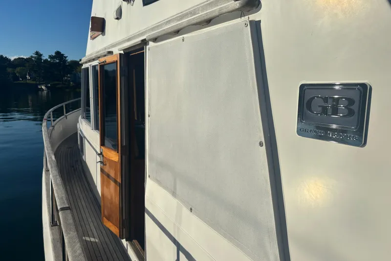Slide: The Image of 1989 Grand Banks 46 Classic yacht with wooden door and GB logo on calm water. - 58