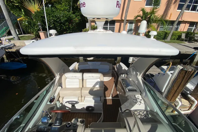 Slide: The Image of 2012 Sea Ray 330 Sundancer yacht interior with seating and helm, docked near palm trees. - 13