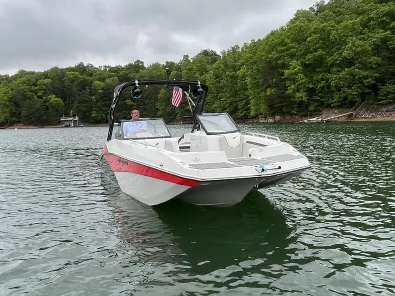 Slide: The Image of A 2025 Starcraft SVX OB 230 DC OB boat on a calm lake. It's white with red accents and has an American flag at the stern. - 2