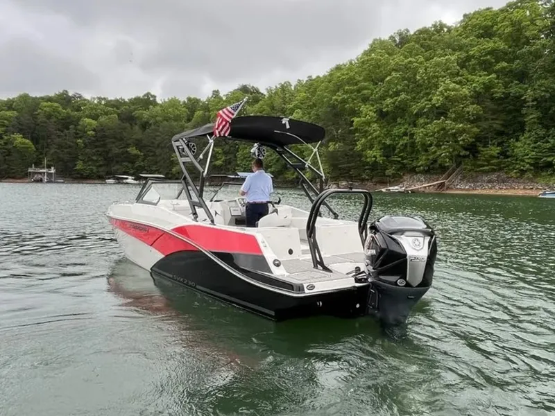Slide: The Image of A 2025 Starcraft SVX OB 230 DC OB boat on a calm lake with wooded shores. - 6