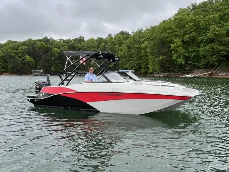 Slide: The Image of A 2025 Starcraft SVX OB 230 DC OB boat on a calm lake, surrounded by trees. - 17