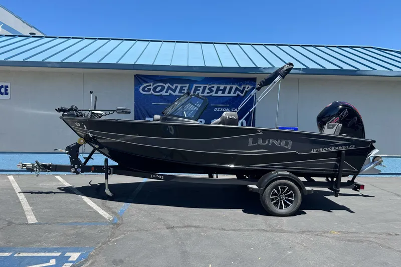 The Image of 2026 Lund 1875 Crossover XS boat on trailer, parked outside a building. - 0