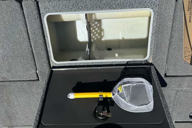 Slide: The Image of 2026 Lund 1875 Crossover XS boat storage compartment with fishing net and yellow handle. - 16