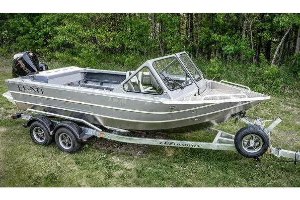 The Image of 2026 Lund 200 Heavy Gauge boat on trailer, parked on grass with forest background. - 1