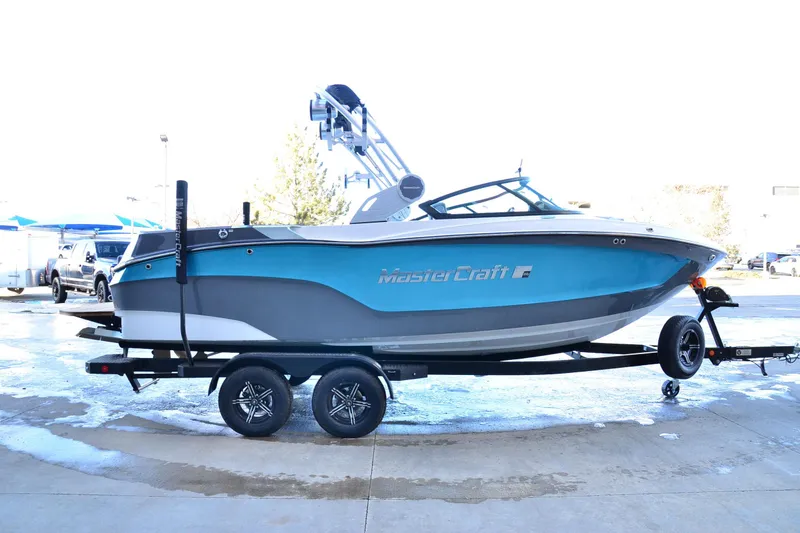 Slide: The Image of 2023 MasterCraft XT22 T boat on trailer, blue and gray design, parked outdoors. - 6