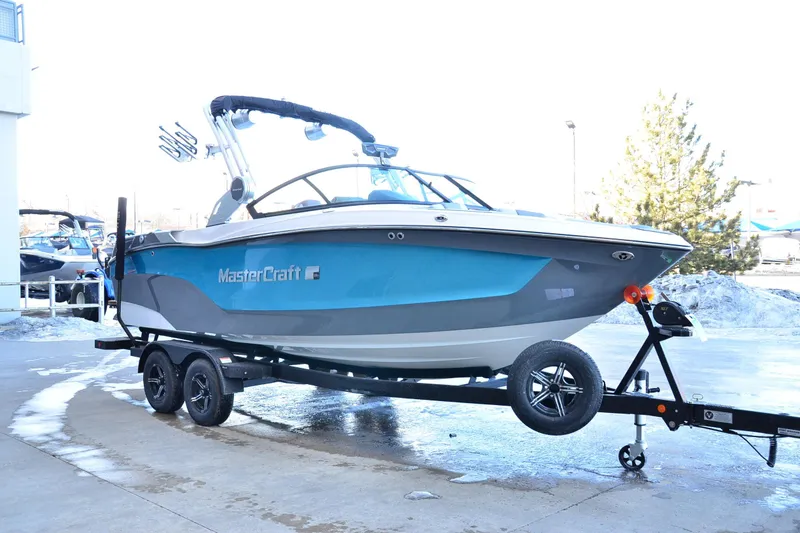 Slide: The Image of 2023 MasterCraft XT22 T boat on trailer, blue and gray design, parked outdoors. - 7