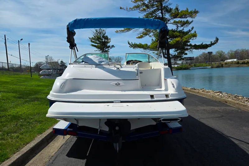 Slide: The Image of 2006 Glastron DX 235 boat with blue canopy, parked near a serene lake. - 2