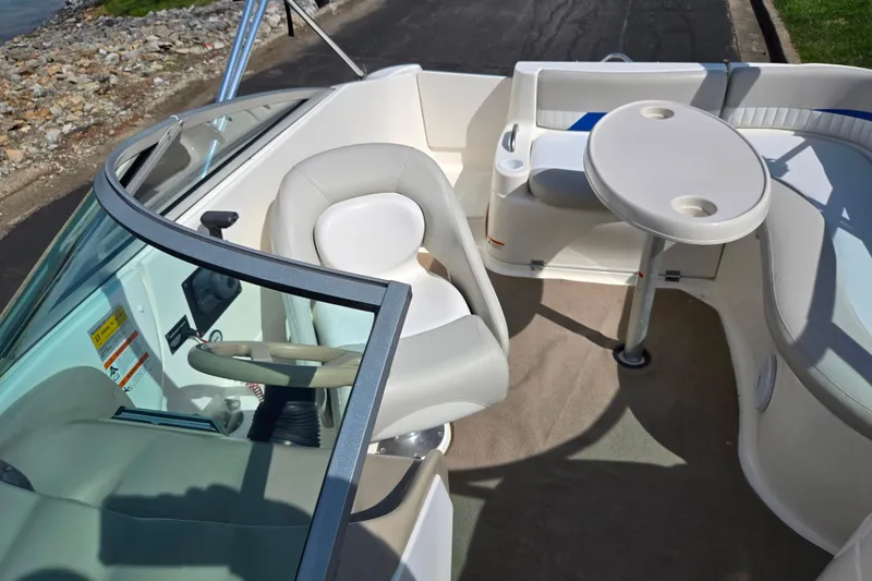 Slide: The Image of 2006 Glastron DX 235 boat interior with seating and table, docked by a rocky shoreline. - 22