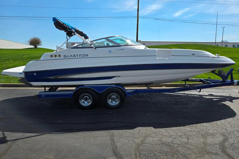 Slide: The Image of 2006 Glastron DX 235 boat on trailer, white and blue design, parked outdoors. - 4