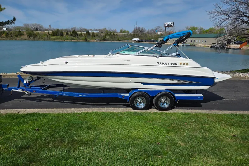 Slide: The Image of 2006 Glastron DX 235 boat on trailer by a lake, featuring sleek design and blue accents. - 9