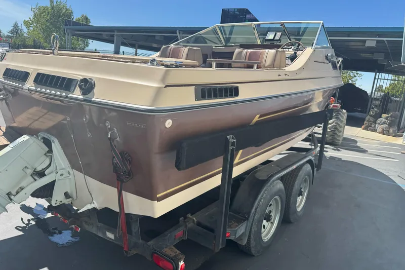 Slide: The Image of 1985 Invader 20 boat on trailer, brown and beige, parked outdoors under clear sky. - 8