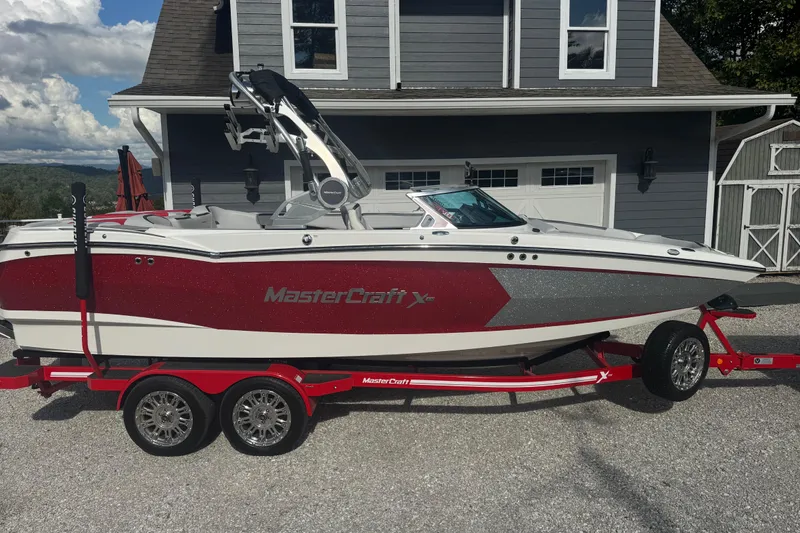 The Image of 2020 MasterCraft XStar boat on a red trailer, parked in front of a gray house. - 1
