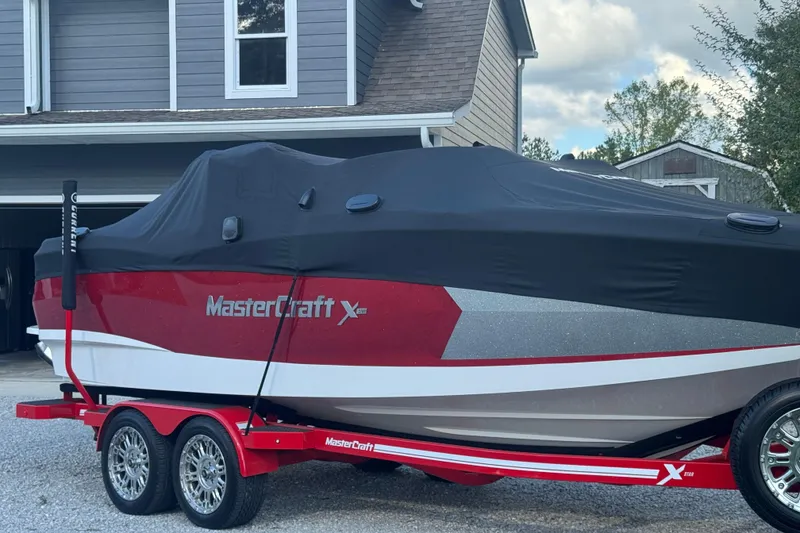 Slide: The Image of 2020 MasterCraft XStar boat covered on a red trailer in a driveway. - 7