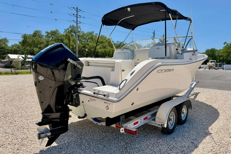 Slide: The Image of 2023 Cobia 220 Dual Console boat with Mercury engine on trailer, parked outdoors. - 5