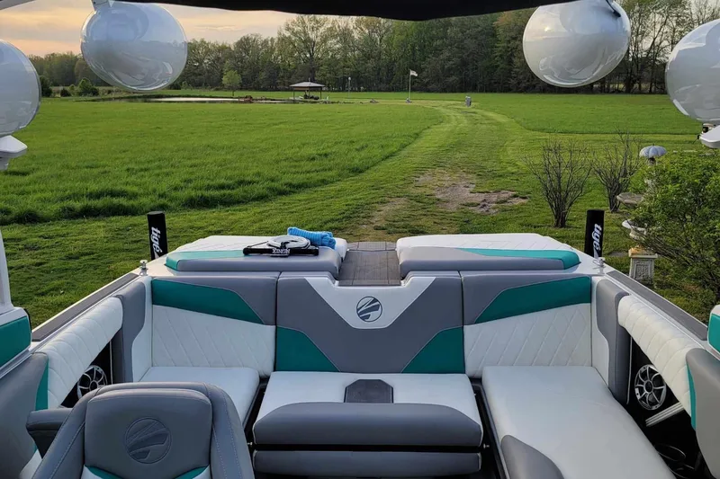 Slide: The Image of 2022 Tigé Z1 boat interior with plush seating, set against a lush green landscape. - 12