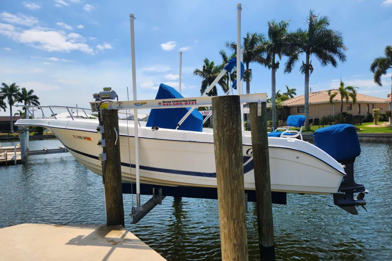 The Image of 2001 Cobia 234 Center Console boat on lift, surrounded by palm trees and waterfront homes. - 0
