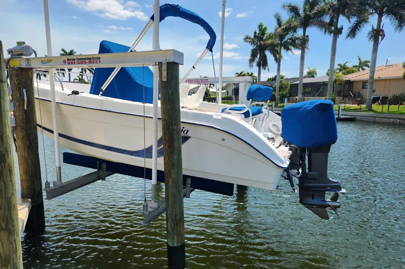 Slide: The Image of 2001 Cobia 234 Center Console boat on lift by waterfront homes and palm trees. - 3