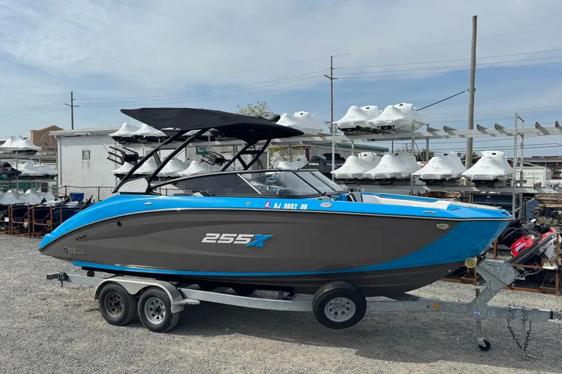 The Image of 2022 Yamaha Boats 255XD on trailer, blue and gray design, parked in marina. - 0