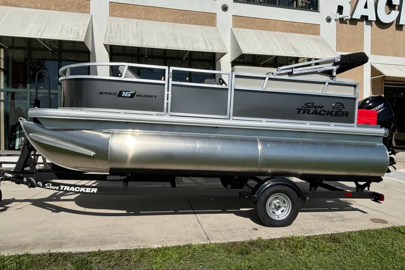 The Image of 2026 Sun Tracker Bass Buggy 16 XL Select pontoon boat on trailer, parked outdoors. - 0