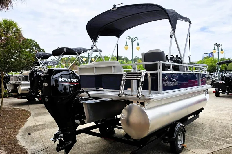 Slide: The Image of 2026 Sun Tracker Bass Buggy 16 XL Select pontoon boat with Mercury engine, parked outdoors. - 2