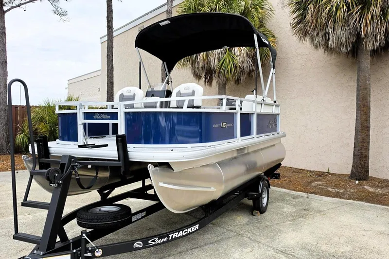 Slide: The Image of 2026 Sun Tracker Bass Buggy 16 XL Select pontoon boat on trailer, parked outdoors. - 3