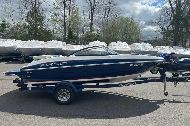 The Image of 2017 Larson LX 185S I/O boat on trailer, parked outdoors with covered boats in background. - 1