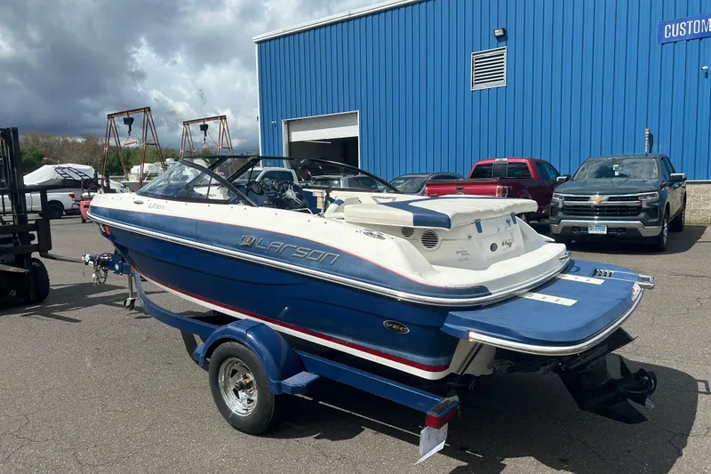 Slide: The Image of 2017 Larson LX 185S I/O boat on trailer, parked near blue building. - 3