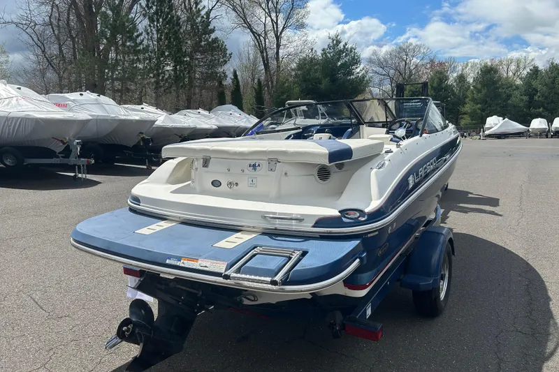 Slide: The Image of 2017 Larson LX 185S I/O boat on trailer, parked outdoors with covered boats nearby. - 4