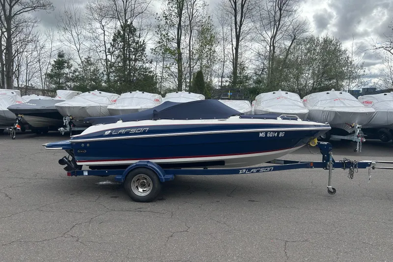 Slide: The Image of 2017 Larson LX 185S I/O boat on trailer, parked outdoors with covered boats in background. - 8