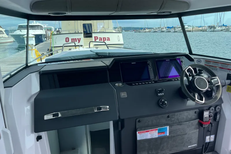 Slide: The Image of 2024 Axopar 37 XC Cross Cabin helm with dual displays, steering wheel, and marina view. - 12