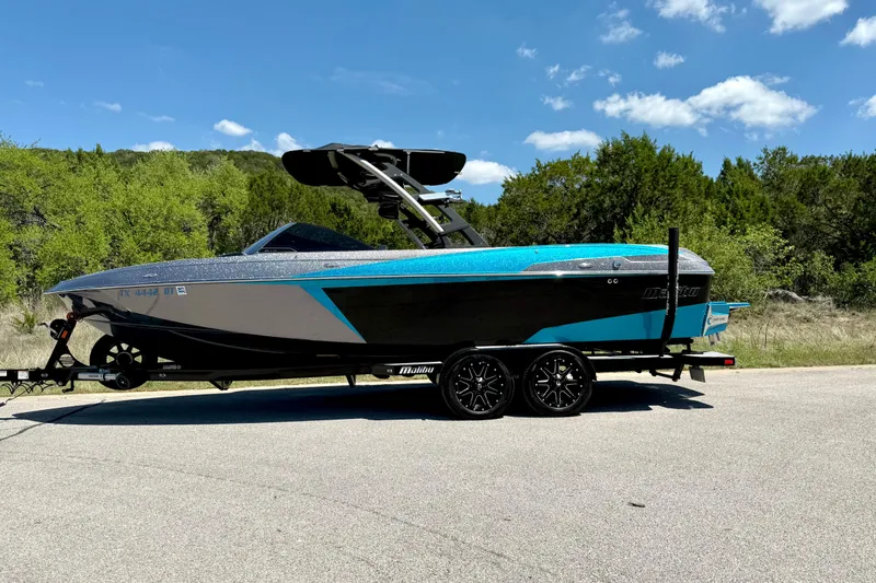 Slide: The Image of 2016 Malibu Wakesetter 25 LSV boat on trailer, parked on road with trees in background. - 11