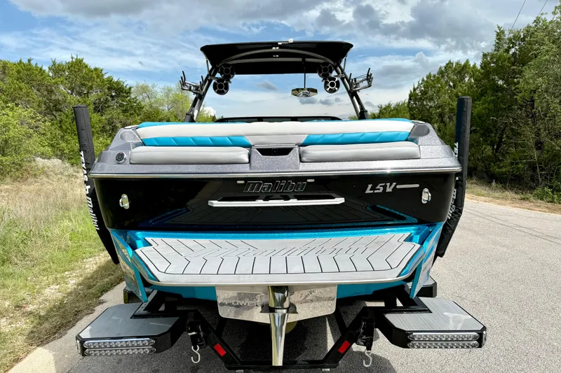 Slide: The Image of 2016 Malibu Wakesetter 25 LSV boat, rear view, parked on a road with trees. - 16