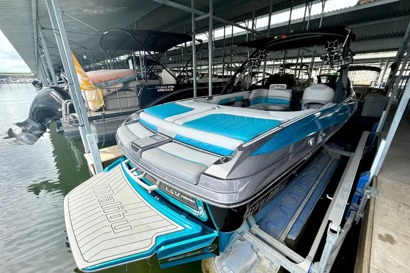 Slide: The Image of 2016 Malibu Wakesetter 25 LSV boat docked in a marina, featuring blue and gray seating. - 18