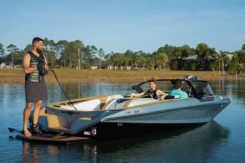 Slide: The Image of Manufacturer Provided Image: 2024 Nautique Ski boat on a lake with people enjoying water sports. - 6