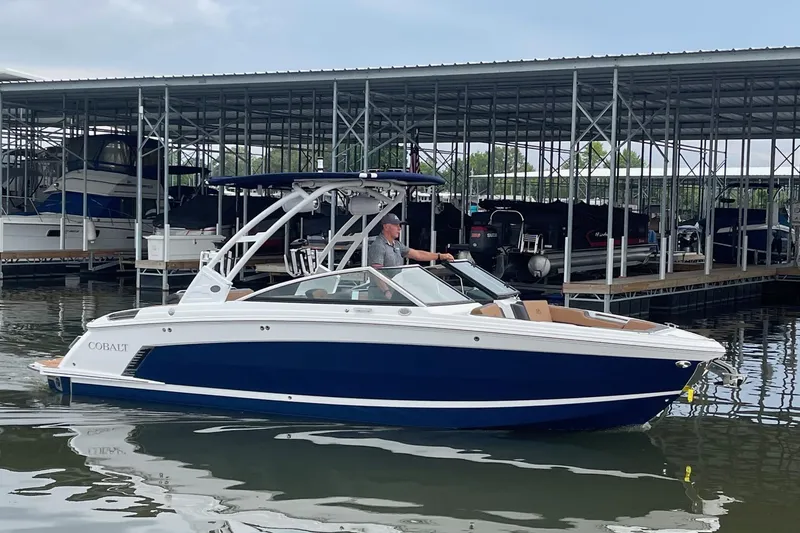 Slide: The Image of 2023 Cobalt R6 Surf boat docked at marina, featuring sleek blue and white design. - 23