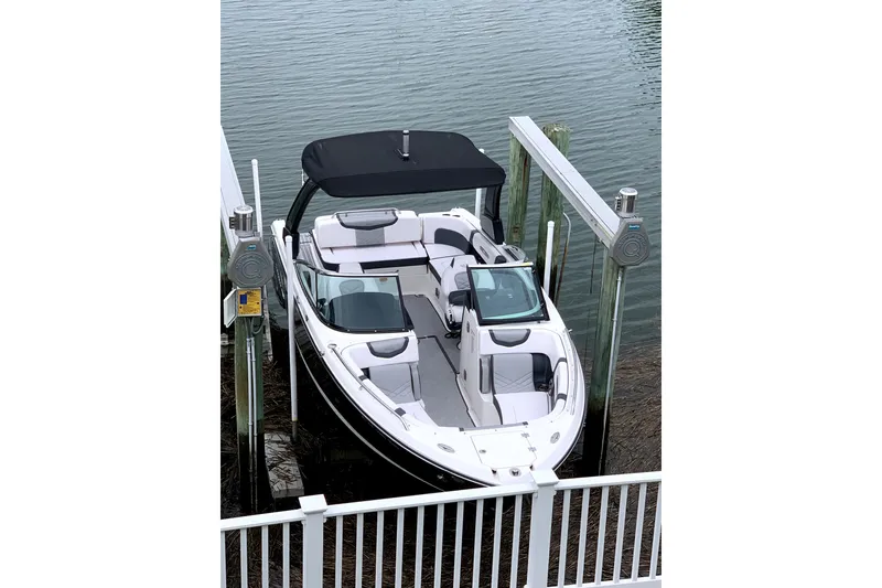 Slide: The Image of 2019 Chaparral 277 SSX boat docked with black canopy on calm water. - 2