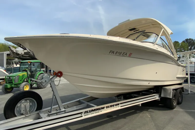 Slide: The Image of 2019 Scout 255 Dorado boat on trailer, parked outdoors with tractor in background. - 5